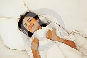 An attractive happy young woman is lying in bed with her eyes closed