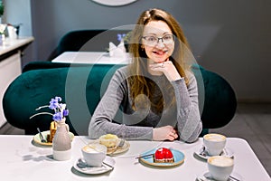 Attractive happy young woman sitting and eating dessert in cafe. Woman wating for her friends in cafe