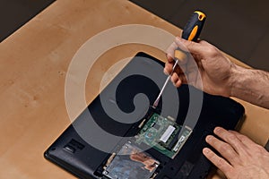 Attractive hardworking guy dismantling laptop with screwdriver, closeup view