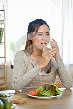 Attractive and healthy Asian woman drinking and sipping a glass of water in the kitchen
