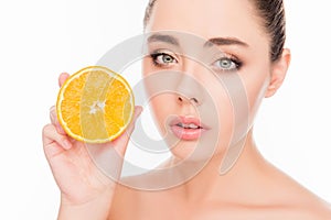 Attractive healthy young woman holding half of orange near her face