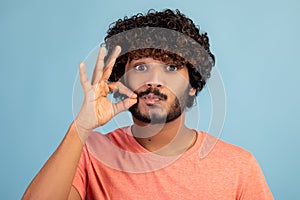 Attractive hindu guy keeping secret, showing zipped lips gesture