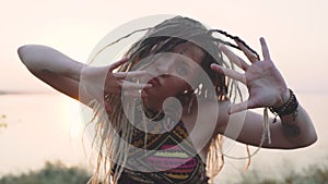 Attractive hippie woman with dreadlocks at sunset having good time and dance outdoors