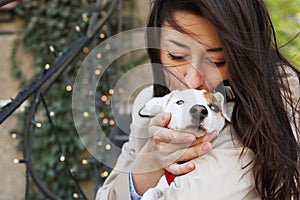 Attractive hipster young woman in sunglasses kissing jack russell terrier puppy in park, green lawn & foliage background. Funny pu