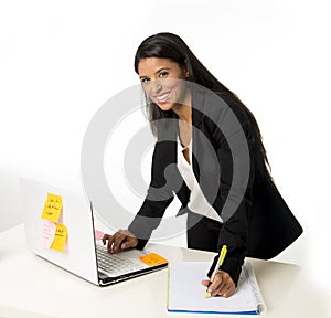 Attractive hispanic businesswoman or secretary taking notes standing leaning on office computer desk