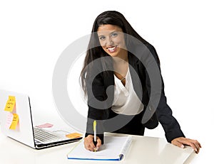 Attractive hispanic businesswoman or secretary taking notes standing leaning on office computer desk