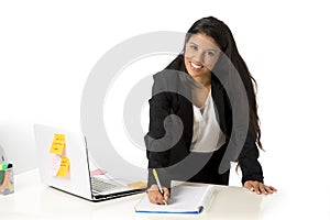 Attractive hispanic businesswoman or secretary taking notes standing leaning on office computer desk