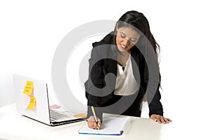 Attractive hispanic businesswoman or secretary taking notes standing leaning on office computer desk