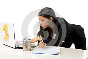 Attractive hispanic businesswoman or secretary taking notes standing leaning on office computer desk