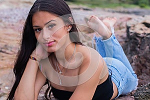 Attractive Hispanic female wearing a strapless crop top lying on rocks