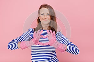 Attractive housewife woman wear rubber cleaning gloves and casual blue striped sweater makes heart gesture over cest, body