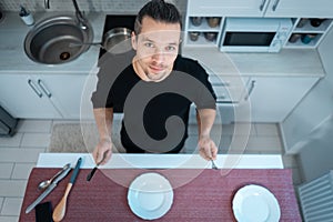 attractive hungry young man on modern kitchen with empty plate, fork and knife