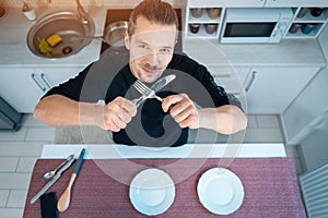 attractive hungry young man on modern kitchen with empty plate, fork and knife