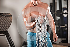 Attractive hunky black male bodybuilder doing bodybuilding pose in gym with iron chains