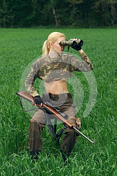 Attractive hunter girl with hunting carbine looking into binoculars