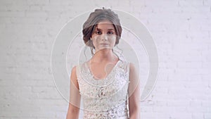 Attractive image of dark-haired bride with neat, gentle hairstyle, goes and looks directly at camera, spinning in long