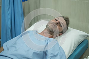 Attractive injured man lying on hospital bed receiving treatment feeling sick and unwell after suffering accident or serious