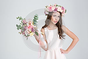 Attractive irritated woman in rose wreath showing bouquet of flowers