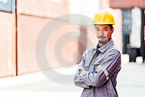 Attractive Japanese man industrial engineer in yellow hard hat, safety uniform with a blurred container yard in background.