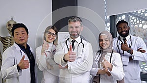 Attractive joyful high-skilled mixed race medical stuff posing on camera and making sign OK
