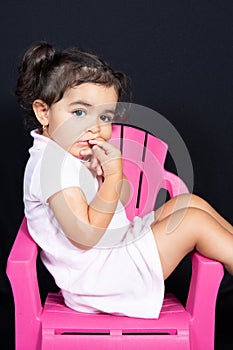 Attractive kid child girl site on pink chair seat on black background