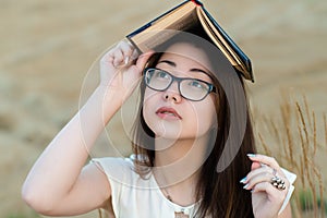 Attractive Korean girl with glasses covers head with book