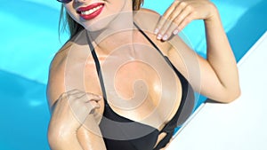 Attractive lady in black bikini stroking breast, sunbathing in swimming pool