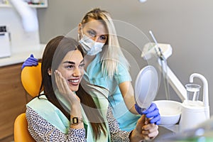 Attractive lady checking her beautiful smile in mirror after stomatological treatment