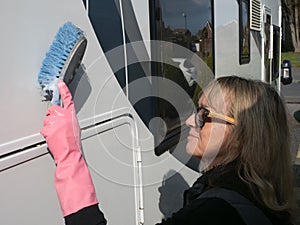 Attractive lady hand cleans her motorhome recreational vehicle with a blue brush.She wears pink rubber gloves and sunglasses