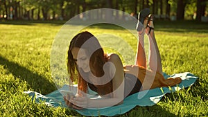 Attractive lady laying down over green grass while typing a message on phone