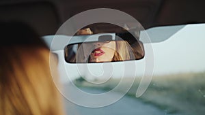 Attractive lady looking in rear view mirror and applying red lipstick in car