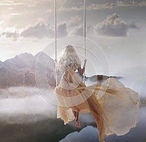 Attractive lady sitting on the swing above the calm lake