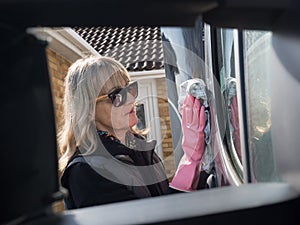 Attractive lady smiling is framed through wing mirror brackets using a cloth to wipe her motorhome recreational vehicle.