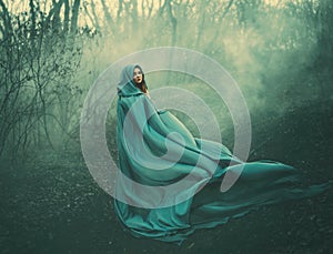 Attractive large lady in long blue summer light waving raincoat runs through forest with bare trees and mysterious white