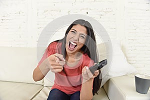 Attractive latin woman at home sofa couch laughing and smiling happy watching television