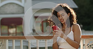 Attractive latino woman with brunette hair using smartphone while standing at city street. Crop view of cheerful female