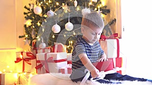 Attractive little boy unwrapping Christmas gifts. Kid opening New Year presents at home.