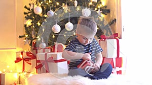 Attractive little boy unwrapping Christmas gifts. Kid opening New Year presents at home.