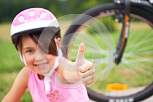 Attractive little cyclist giving thumbs up. Happy joyful little girl with bicycle on the background gesturing thumb up