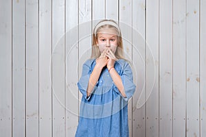 Attractive little girl is covering mouth with two hands not willing to disclose something important. Keep a secret