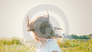 An attractive little girl with long flowing hair twists her head in different directions, the wind develops long hair of