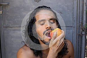 Attractive long haired man eating a peach
