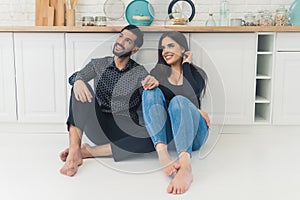 Attractive lovely Couple sitting on the floor in modern kitchen and looking at the window, relationship concept