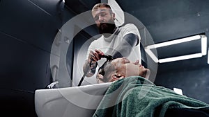 Attractive male is getting a modern haircut in barber shop. Top view of a young man getting his hair washed and his head