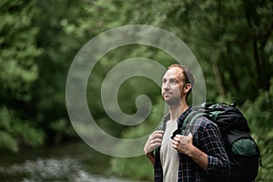 Attractive male hiker with a large backpack standing on the bank of the river