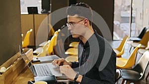 Attractive male in his 20`s wearing glasses and fitness tracker on his wrist, working in a well lit indoors co-working