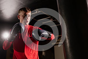 Attractive male punching a bag with boxing gloves. Boxer training in boxing gym