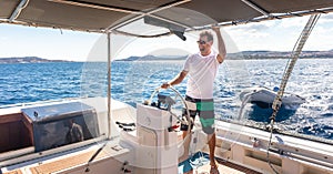 Attractive male skipper navigating the fancy catamaran sailboat on sunny summer day on calm blue sea water.