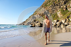 Attractive male surfer walking on beach with surfboard