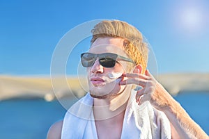 Attractive man applying protective sun cream (solar cream, sunscreen)  to face with finger during vacation.